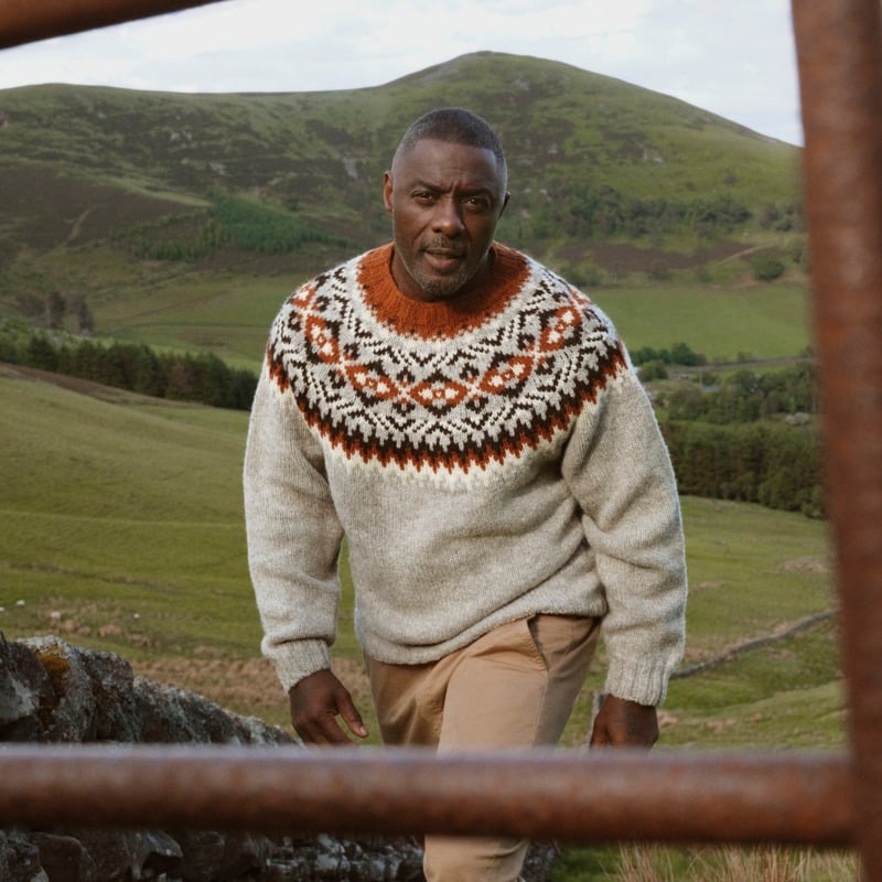 Idris Elba wears a patterned wool sweater and tan trousers in the Pentland Hills for Barbour.