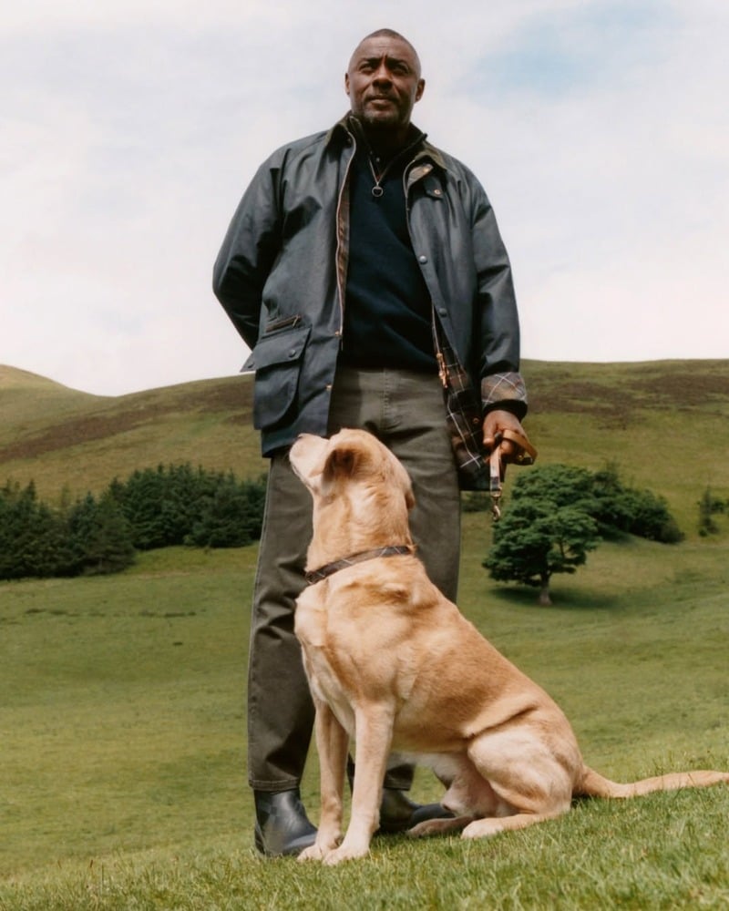 Idris Elba stands beside a dog in a waxed jacket and boots for Barbour.