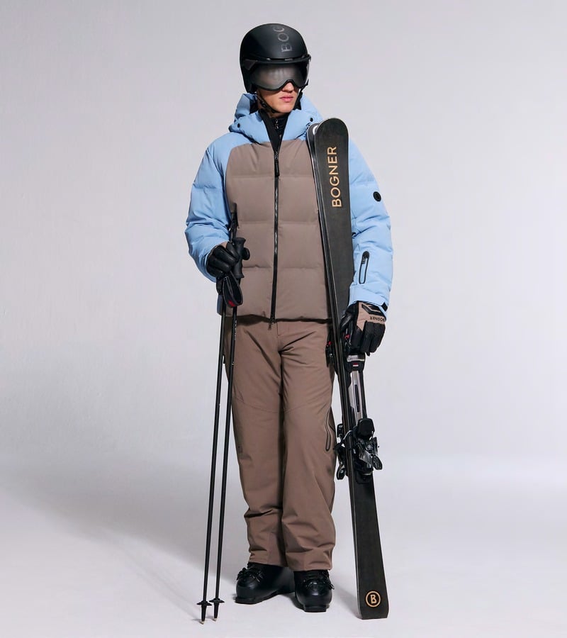 A model in a taupe ski vest over a blue jacket with matching taupe ski trousers and a helmet. Bogner fall-winter 2026 collection.