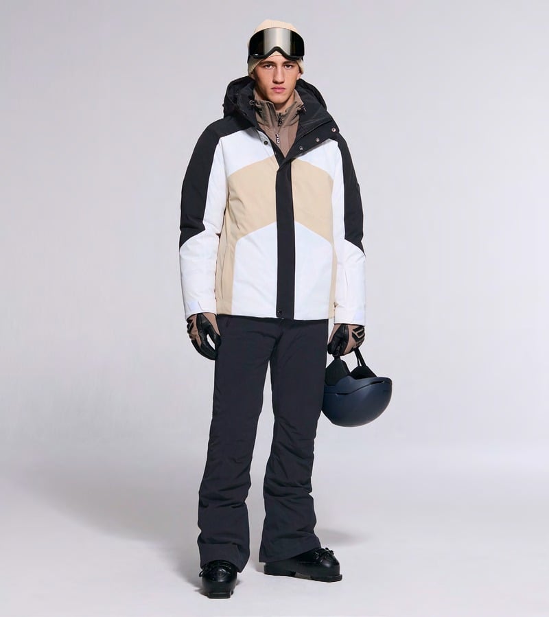 A model wears a white, beige, and black ski jacket with dark trousers and goggles. Bogner fall-winter 2026 collection.