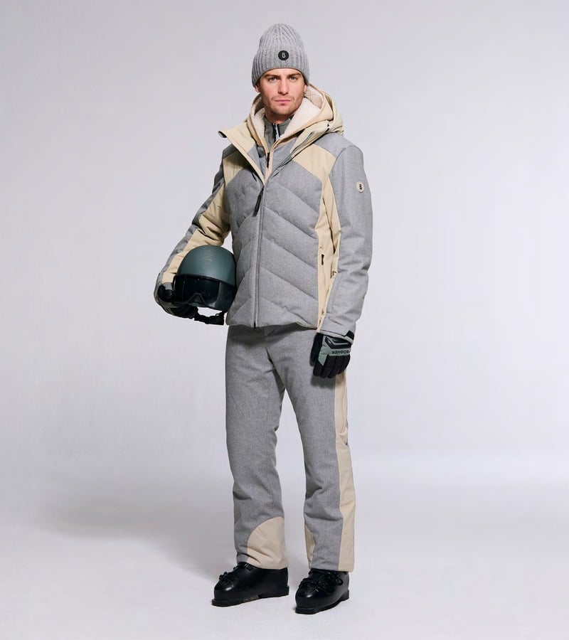 A model wears a gray ski outfit with beige panels and holds a helmet. Bogner fall-winter 2026 collection.