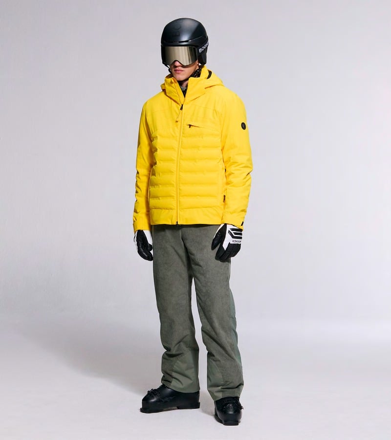 A model wears a bright yellow padded ski jacket with olive trousers and a helmet. Bogner fall-winter 2026 collection.