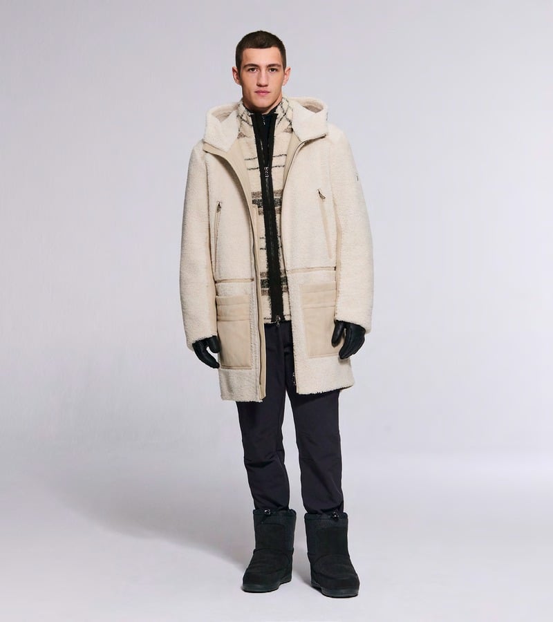 A model wears a long cream coat with dark trousers, gloves, and black boots. Bogner fall-winter 2026 collection.