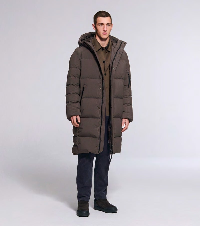A model wears a long brown padded coat over dark trousers and boots. Bogner fall-winter 2026 collection.