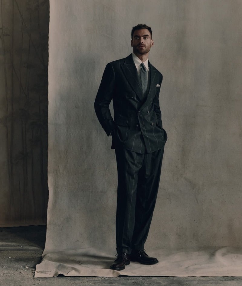 George Alsford wearing a dark double-breasted suit and tie against a studio backdrop for Brunello Cucinelli Winter Edit