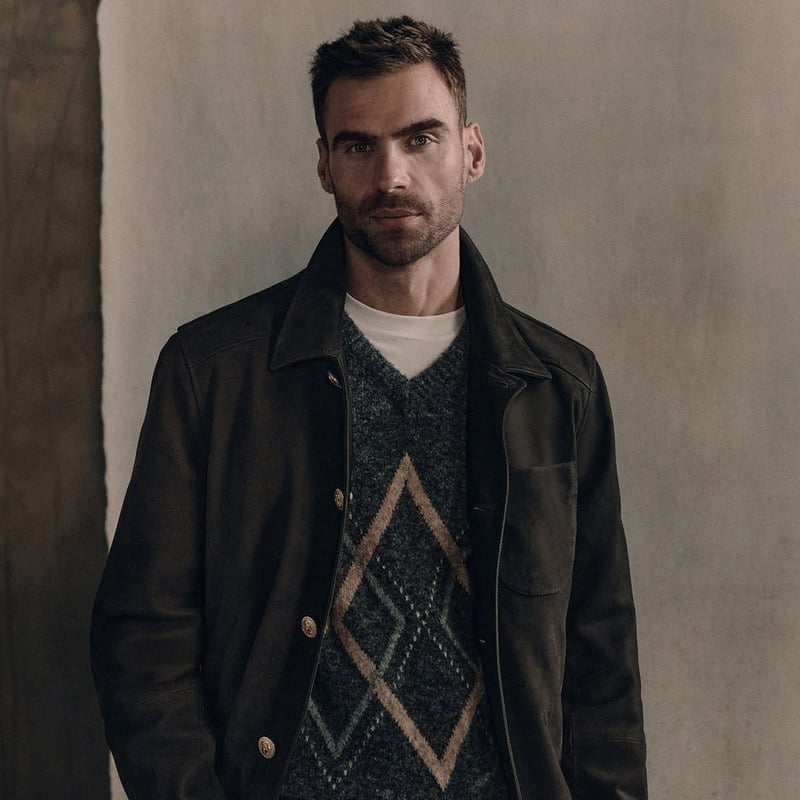 George Alsford in a dark jacket and diamond-pattern V-neck sweater over a white T-shirt for Brunello Cucinelli Winter Edit