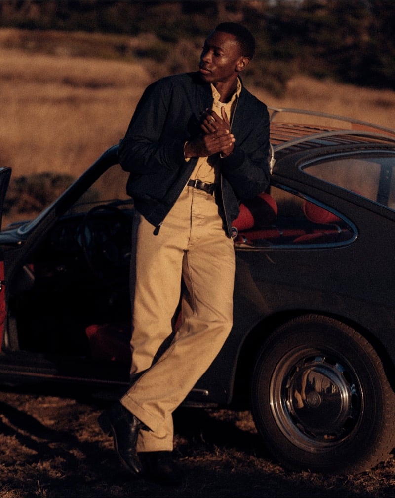 Akin Jaiye wears a bomber jacket and chinos beside a vintage car.