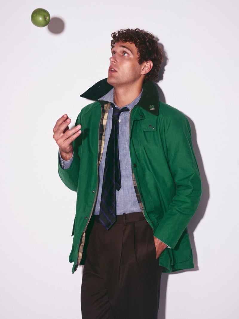 Conor Fay looking up at a green apple tossed in the air, his green Beaufort jacket open to show a tartan lining over a chambray shirt and striped tie