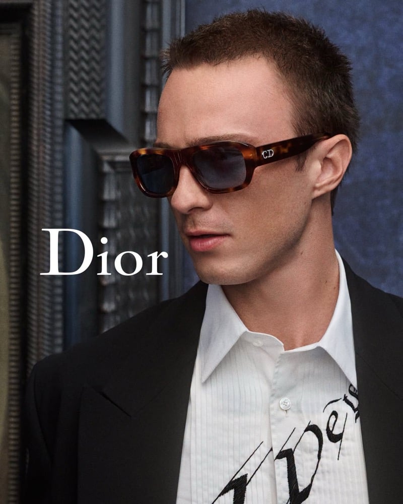 Drew Starkey wearing tortoiseshell sunglasses, a black jacket, and a white printed shirt.