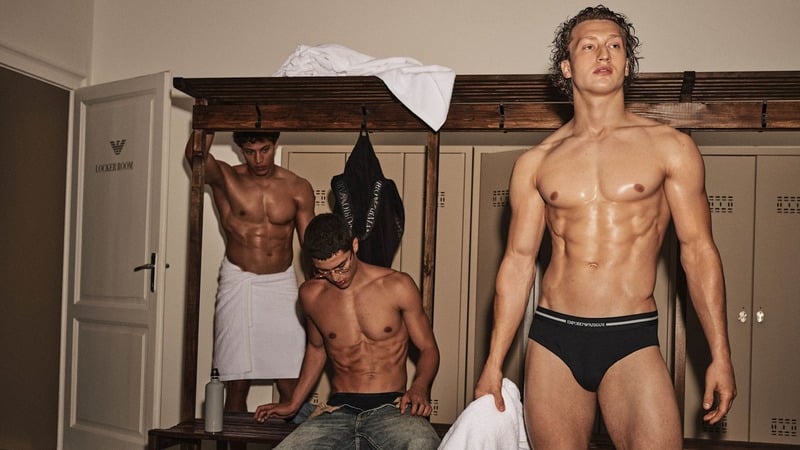 Brennan Aldred in dark Emporio Armani briefs standing in a locker room with other models.