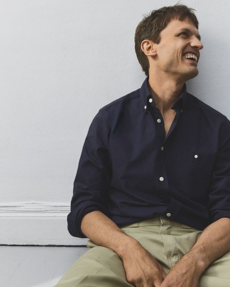 Eddie Klint sits in a navy Oxford shirt with rolled sleeves and khaki trousers