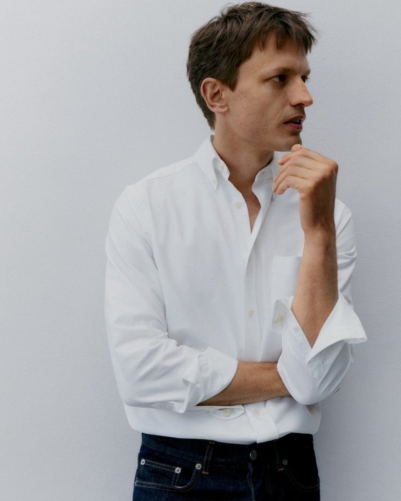 Eddie Klint wears a white Oxford shirt tucked into dark denim, with his sleeves rolled up