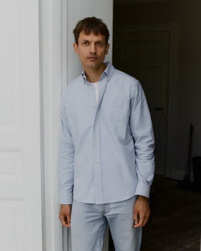 Eddie Klint wears a light blue Oxford shirt open over a white T-shirt with pale jeans