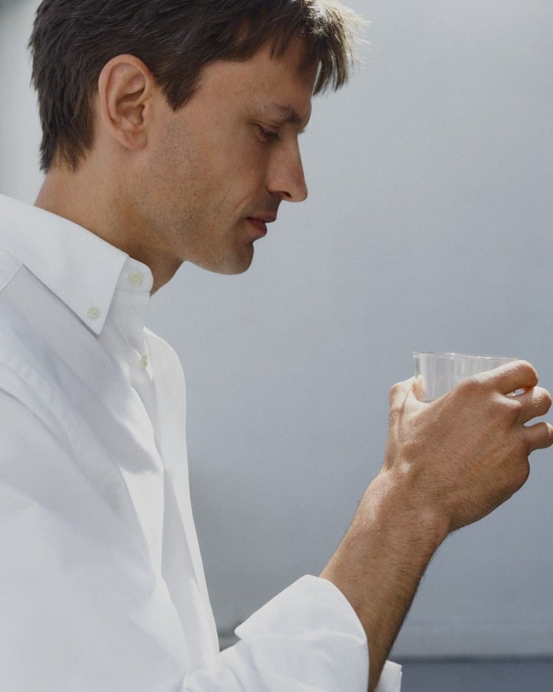 Eddie Klint holds a glass while wearing a white button-down Oxford shirt