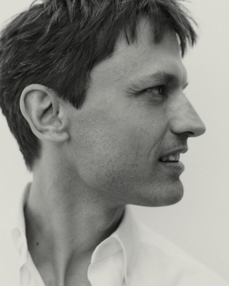 Eddie Klint appears in a black-and-white close-up wearing a white Oxford shirt