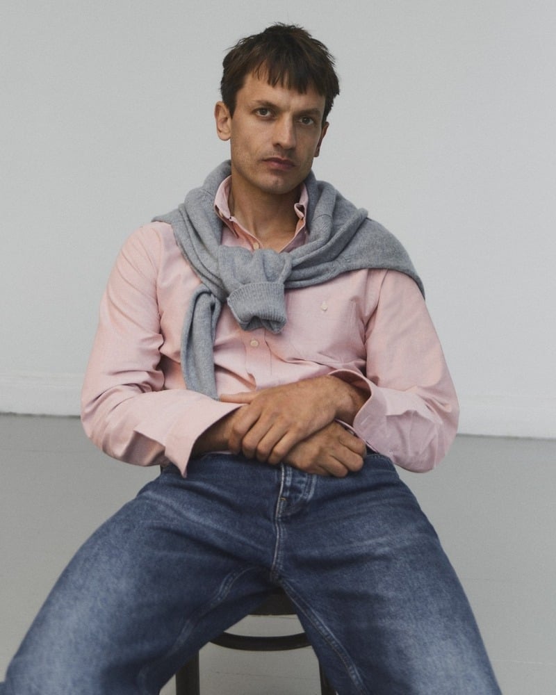 Eddie Klint sits in a pink Oxford shirt and blue jeans with a gray sweater draped over his shoulders