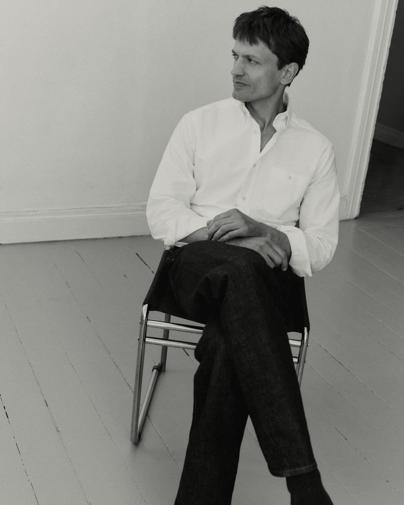 Eddie Klint sits on a chair in a white Oxford shirt and dark jeans