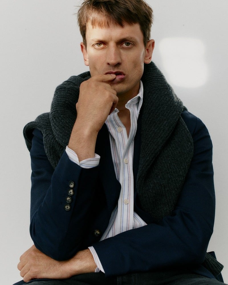 Eddie Klint wears a striped Oxford shirt under a dark jacket with a sweater around his shoulders
