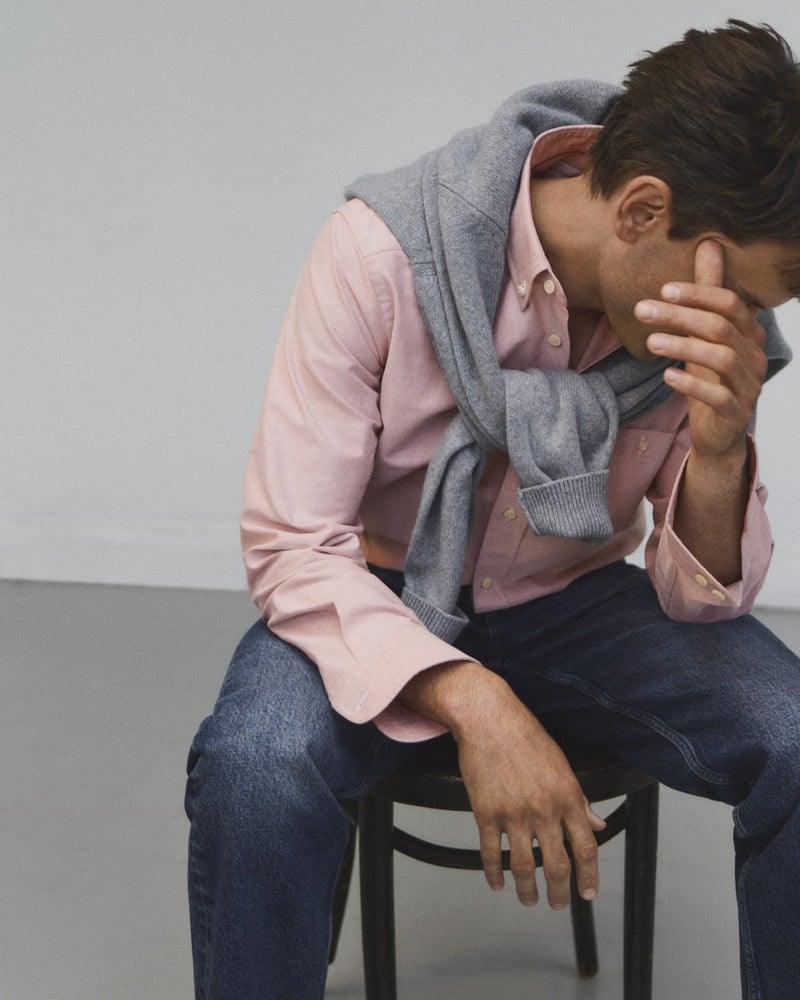Eddie Klint leans forward in a pink Oxford shirt and jeans with a gray sweater over his shoulders