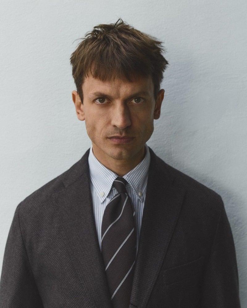 Eddie Klint wears a striped blue Oxford shirt and striped tie beneath a dark tailored jacket