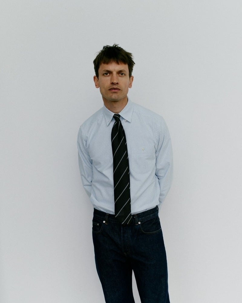 Eddie Klint wears a blue striped Oxford shirt with a dark striped tie and dark jeans