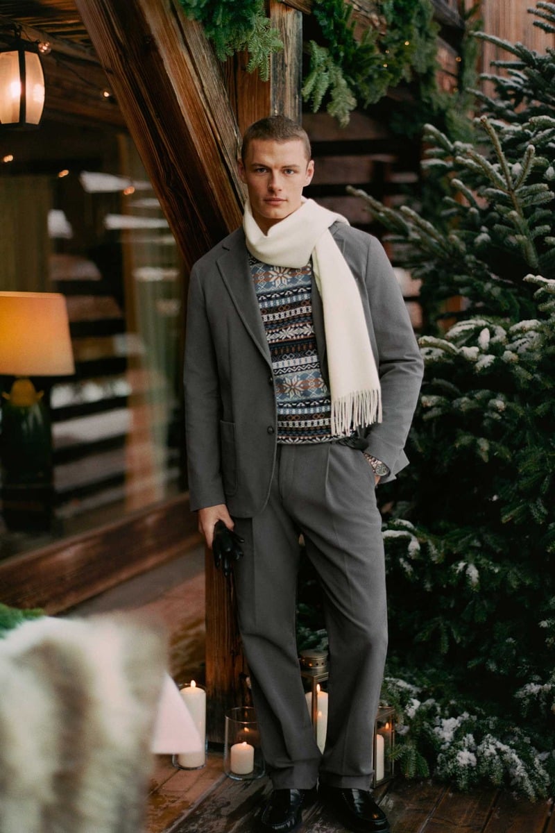 Finley Prentice wears a gray suit with Fair Isle knitwear, a white scarf, and black loafers outside a lodge.