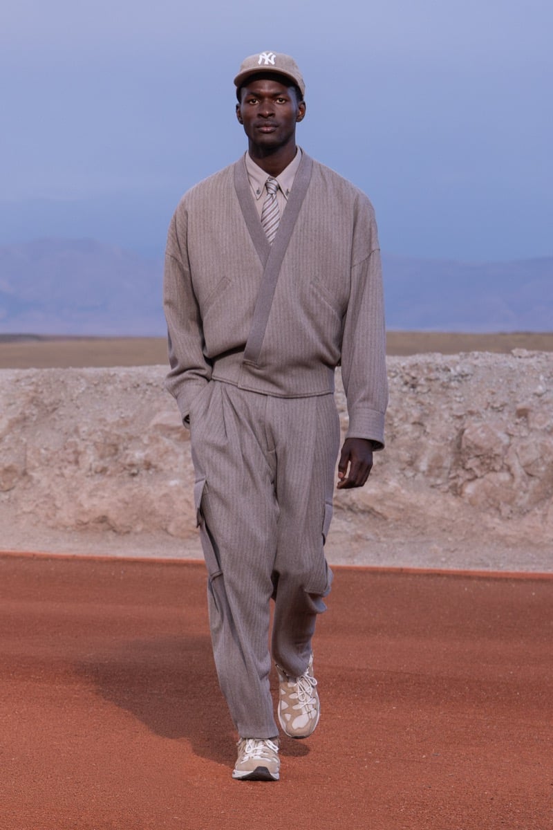 Model wears a taupe wrap jacket, matching wide-leg trousers, a Yankees cap, and sneakers at the Giorgio Armani x Kith fall-winter 2026 show.