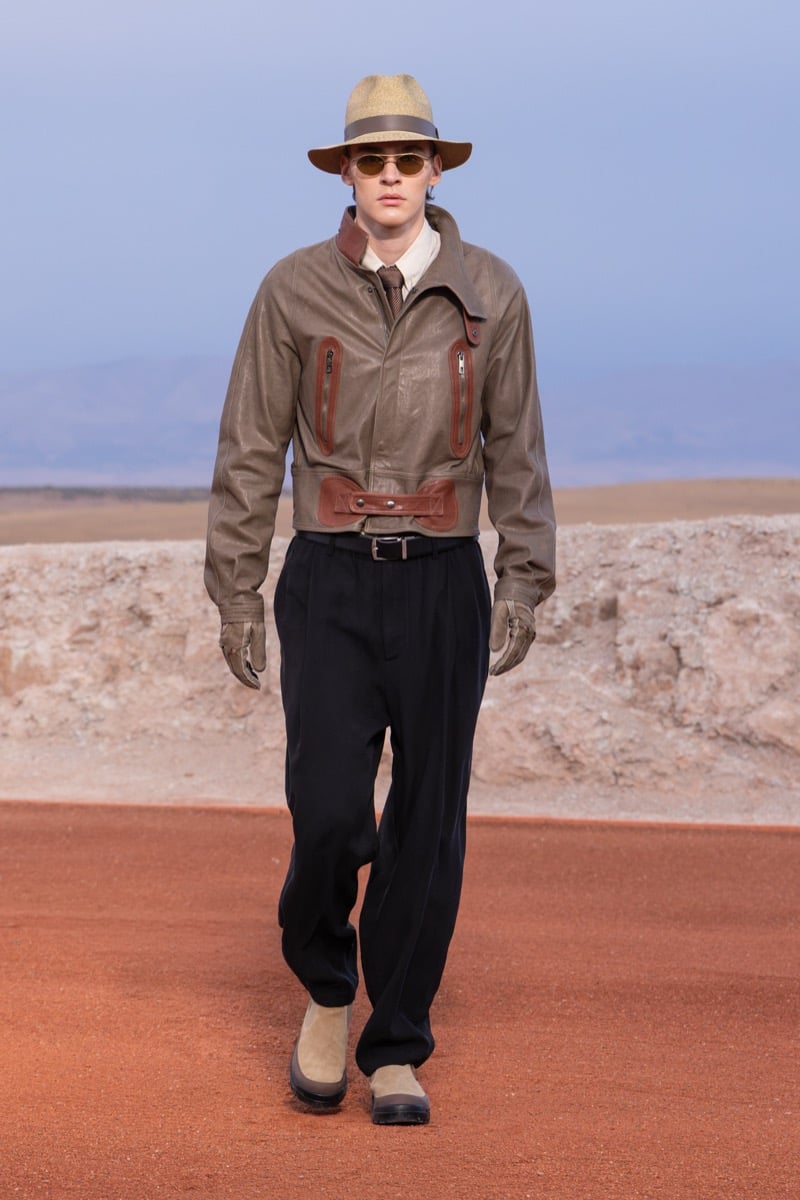 Model wears a brown leather jacket, black trousers, a tan brimmed hat, and sunglasses at the Giorgio Armani x Kith fall-winter 2026 show.