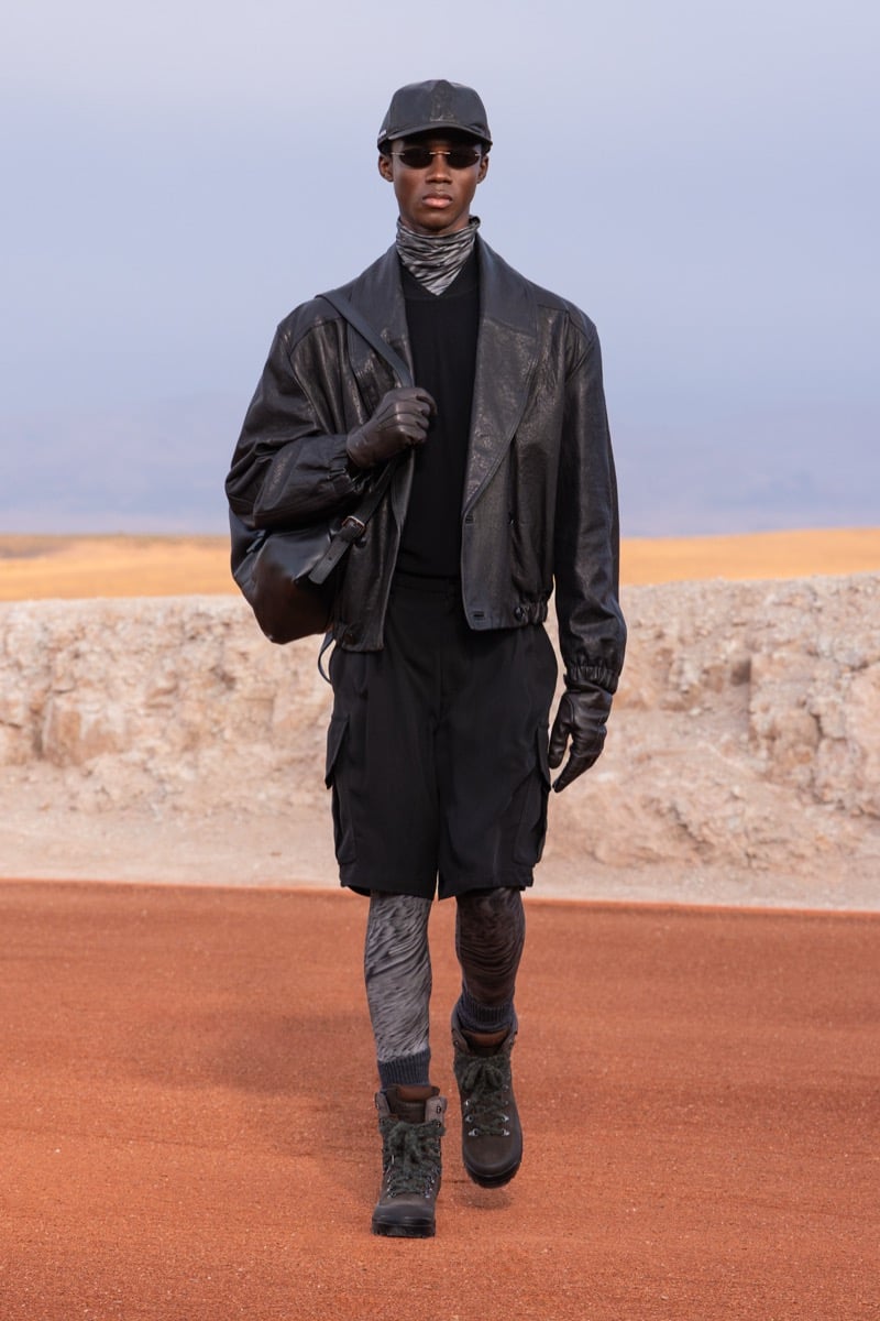 Model wears a black leather jacket, black shorts, a dark cap, and tall boots at the Giorgio Armani x Kith fall-winter 2026 show.
