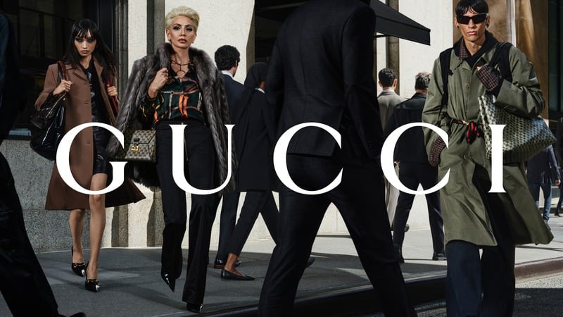 Meng Yu, Sabine Getty and Paul Segurola wear GucciCore on a city sidewalk, including a belted olive trench coat. Gucci logo across the photograph.