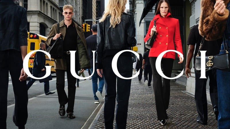 Timo Pan and Alla Kostromichova wear an olive jacket and a red double-breasted coat on a New York sidewalk. Gucci logo across the photograph.