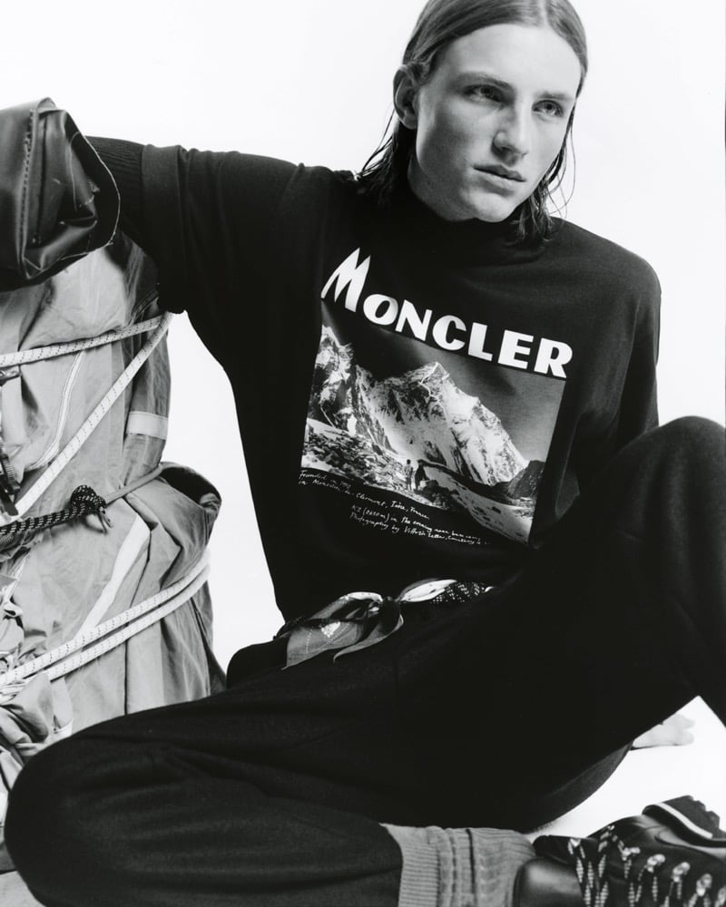 Black-and-white photo of Indiana van't Slot seated in a Moncler sweatshirt printed with a mountain photograph, leaning on a rope-lashed backpack