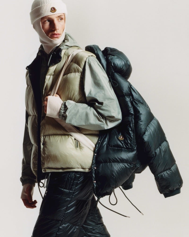 Indiana van't Slot in a knit balaclava and a quilted khaki puffer vest over a sage jacket, a dark green puffer slung over his shoulder and glossy quilted trousers
