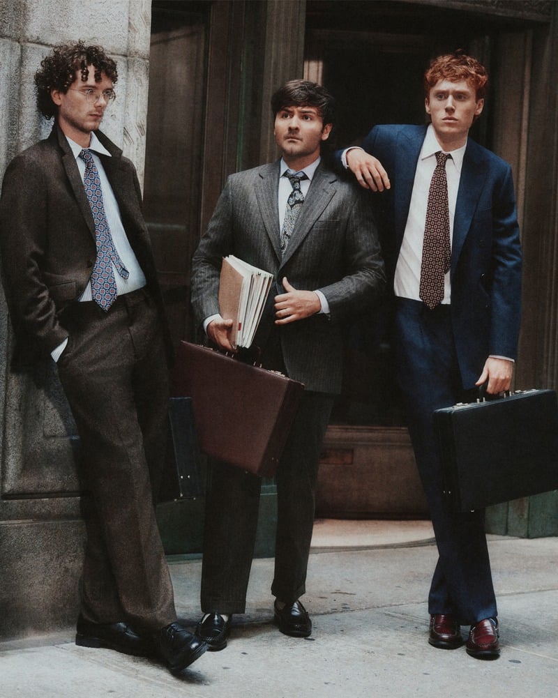 Martin Herlihy, John Higgins, and Ben Marshall wear suits and ties with briefcases on a New York sidewalk.