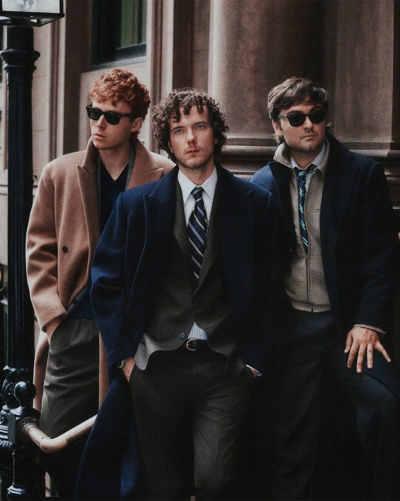 Ben Marshall, Martin Herlihy, and John Higgins wear tailored coats over suits and shirts on a New York sidewalk.