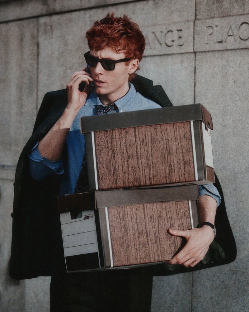 Ben Marshall holds two briefcases against his blue shirt while speaking on a phone.