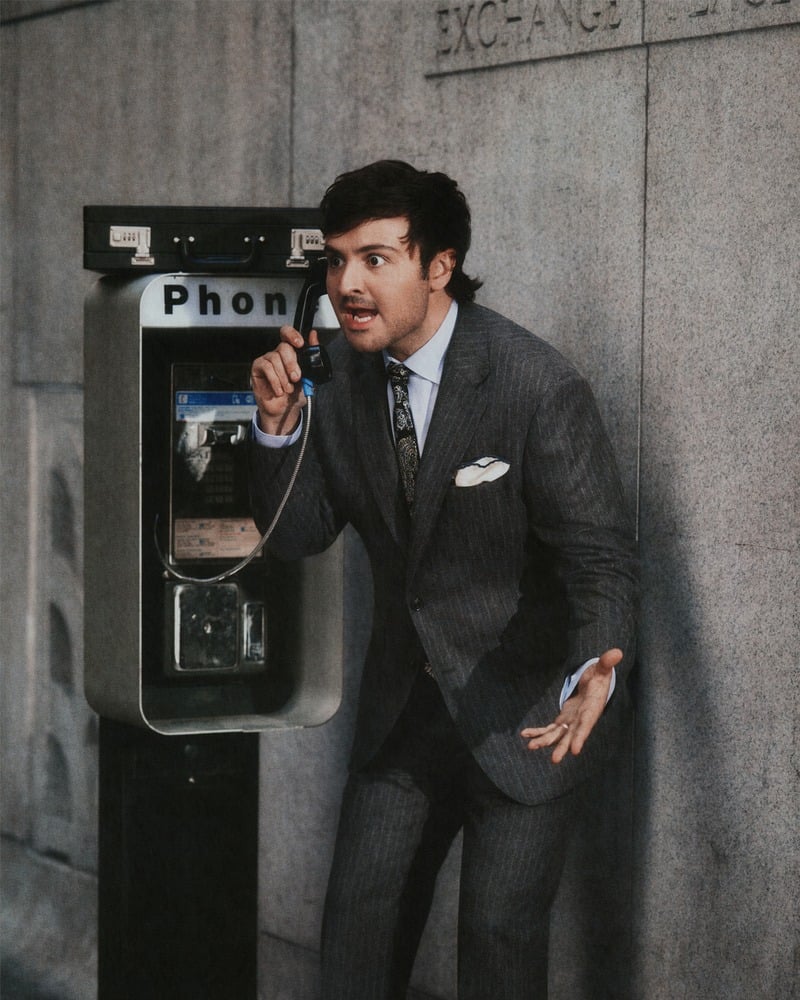 John Higgins speaks at a payphone in a gray suit and patterned tie.