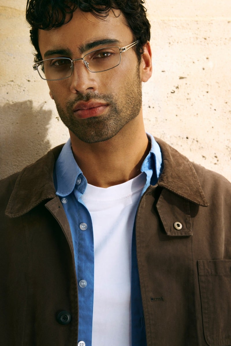 Jy Aoukar wears Jimmy Fairly Jo silver glasses with a brown jacket over a blue shirt and white T-shirt.