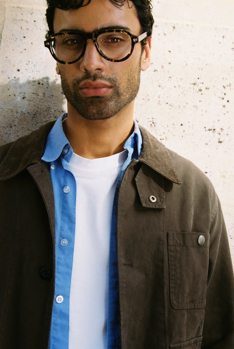 Jy Aoukar wears dark tortoiseshell Jimmy Fairly Sao glasses with a brown jacket and blue shirt.