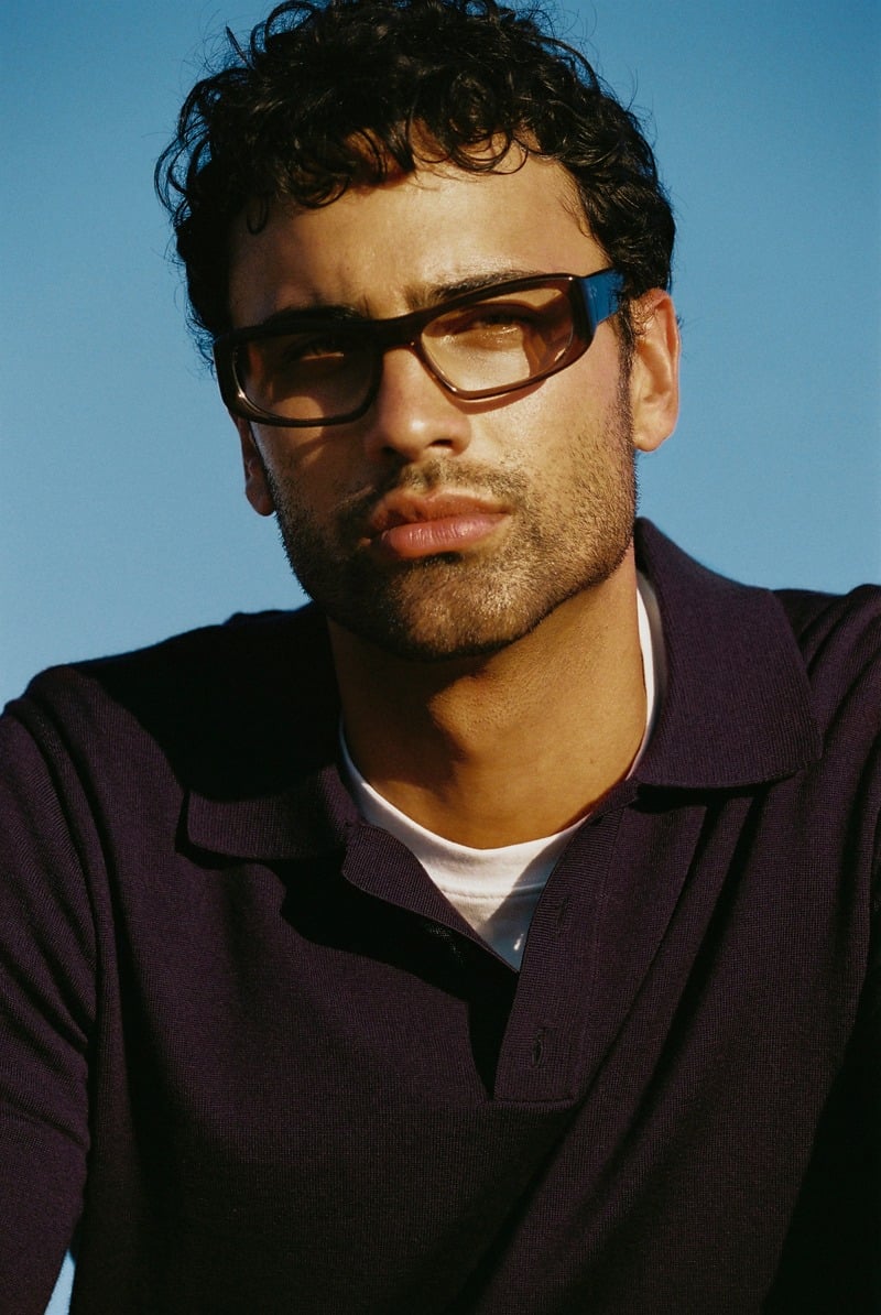 Jy Aoukar wears brown Jimmy Fairly Wesley glasses and a dark polo in the sunlight.
