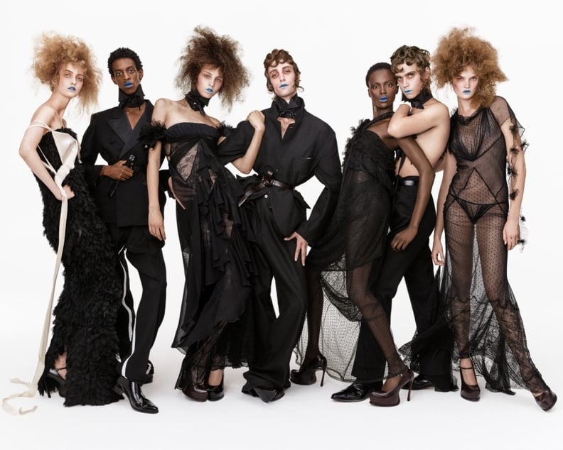Seven models in black ruffles, lace, sheer tulle, and tailoring with blue lips, posed in a row against a white backdrop