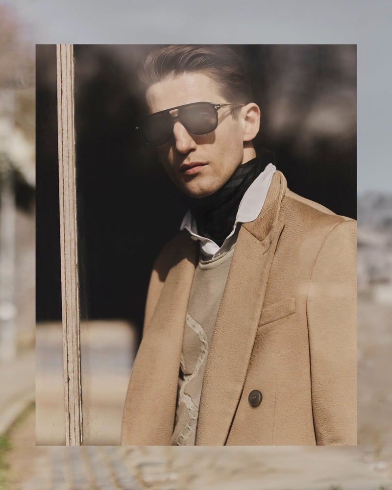 Anatol Modzelewski wears sunglasses and a camel coat in an inset campaign portrait for John Varvatos' fall-winter 2026 campaign