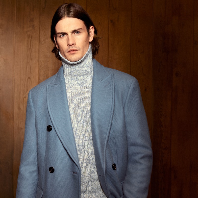 Harrison Page wears a gray double-breasted coat over a marled turtleneck against wood paneling for JOOP!.