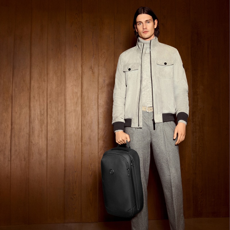 Harrison Page wears a pale blouson and gray tailored trousers, holding a black backpack for JOOP!.
