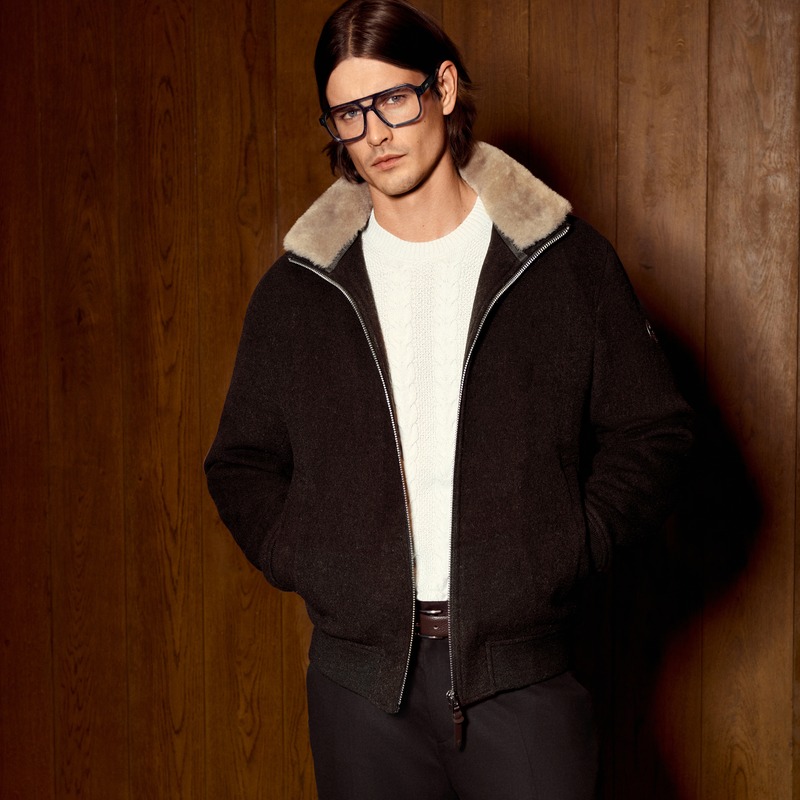 Harrison Page wears dark-rimmed glasses and a dark shearling-collar jacket over a cable-knit sweater for JOOP!.