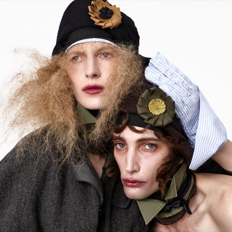 Close-up of Julia Nobis in a rosette-trimmed cap and Thomas Riguelle in a brimmed hat with a light blue gingham glove resting on his shoulder