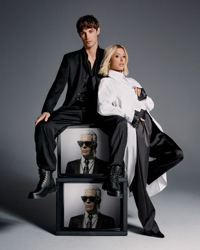Kit Butler and Paris Hilton pose on stacked televisions in black tailoring and an oversized white shirt.