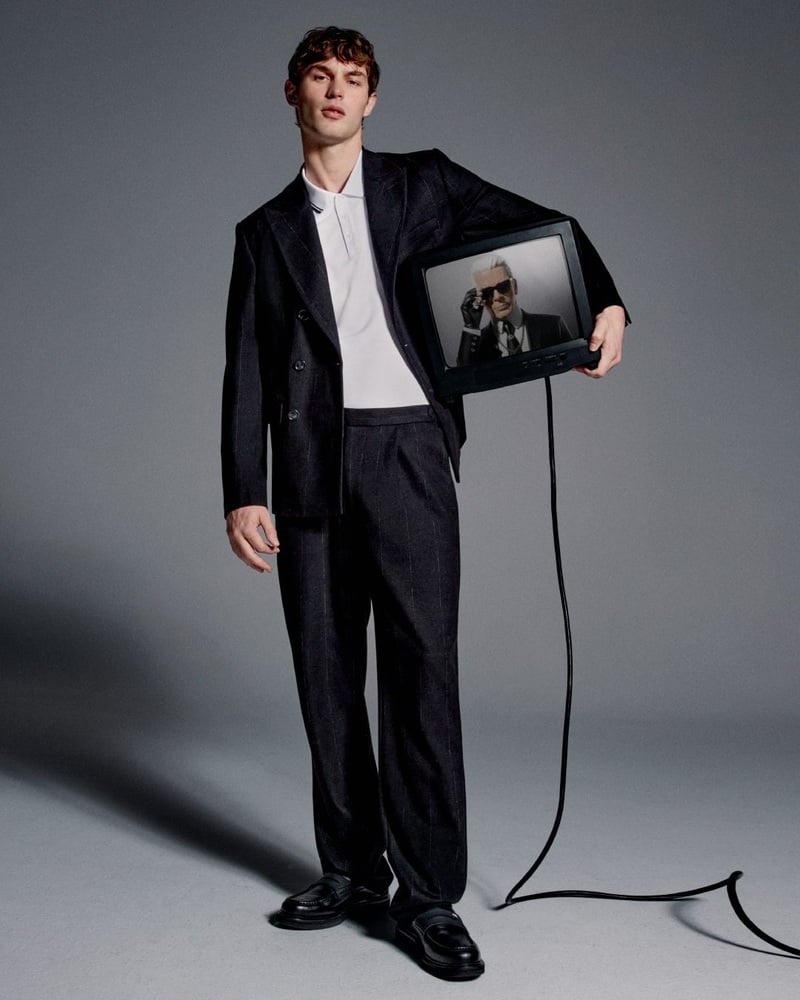 Kit Butler wears a dark suit and white shirt while holding a television showing NOT-KARL.