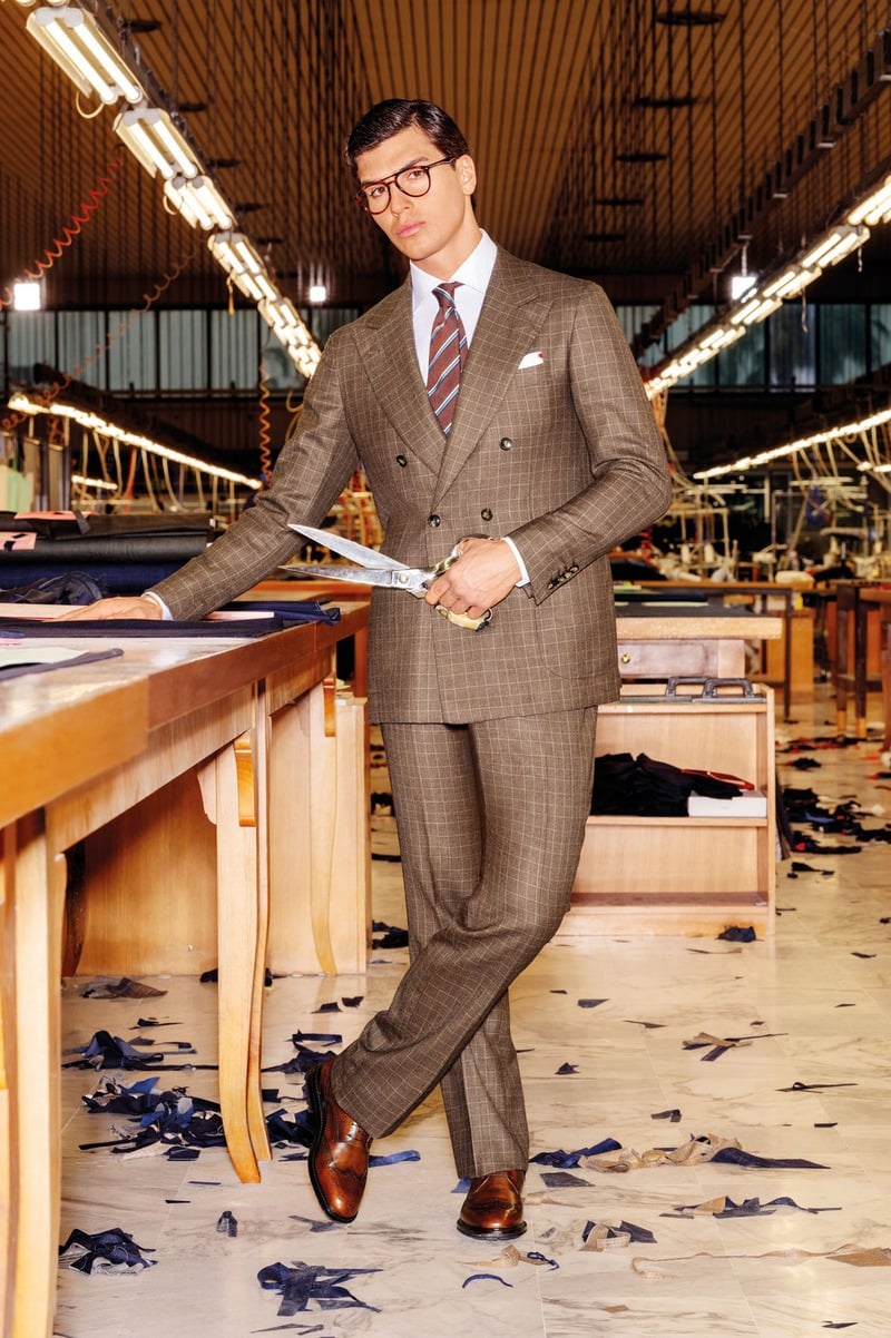 Atila Escolano Sanchez wears a checked double-breasted Kiton suit and holds shears beside a cutting table.
