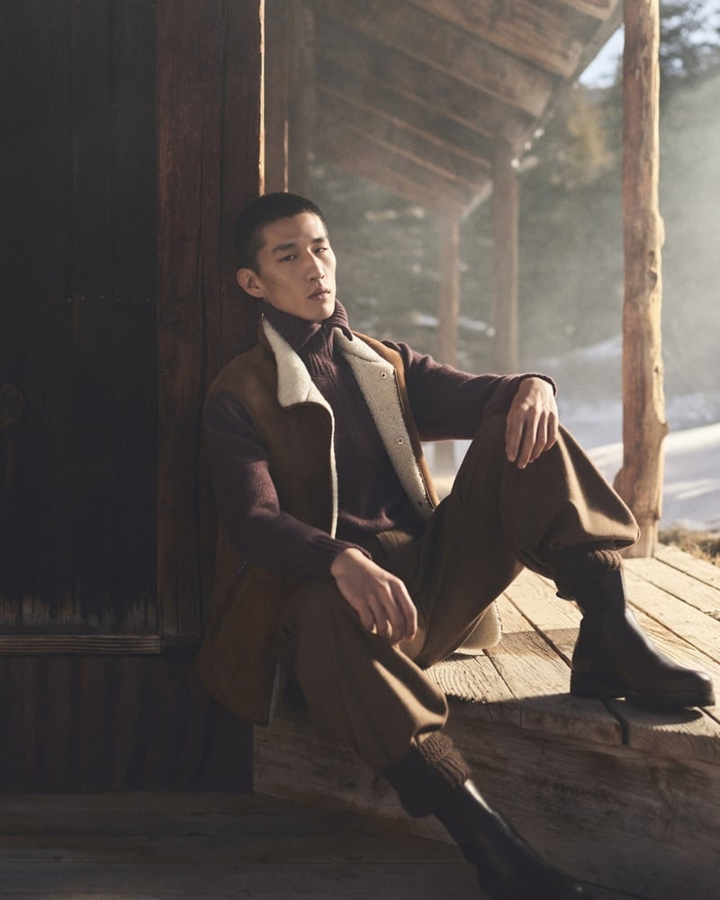 Long Li sits on a wooden porch in brown tailoring and boots for Loro Piana's holiday 2026 campaign.